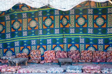 Geleneksel kumaşları ve halıları olan Bedevi çadırı, yere dekore edilmiş ve shisha veya nargile tüttürme masaları.