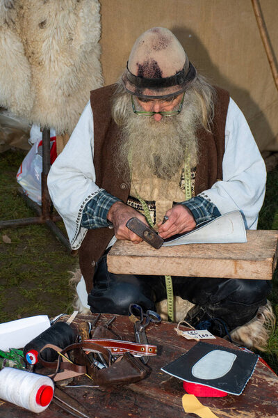 Bucharest, Romania, 25th od December 2019: Old man working with leather and making authentic moccasins shoes