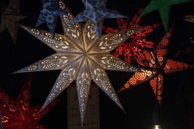 Yılbaşı dekoratif unsurları siyah arka planda şimşek şeklinde yıldız şeklinde güzel kağıt fenerler. Noel pazarında asılı parlak renkli festival yıldızları. Yeni yıl ve Noel konsepti.