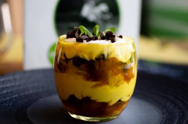 Geleneksel İtalyan tatlı tiramisusu kakao ve nane yapraklarıyla süslenmiş. Koyu mavi ahşap bir masada, kakao, koyu çikolata, kahve çekirdekleri ve nane yapraklarıyla süslenmiş. Boşluğu kopyala