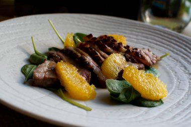 Karamelli narenciye, mandalina, portakal, mango soslu sulu ördek göğsü bifteği, restoran masasında beyaz bir tabakta bebek ıspanağı. Sıcak Et Tabakları. Üst görünüm