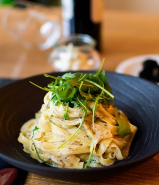 Geleneksel İtalyan tarifi Tagliatelle makarnası siyah mantar orman mantarı soslu, beyaz krem peynirli carbonara soslu restoran masasında siyah bir kasede servis ediliyor.