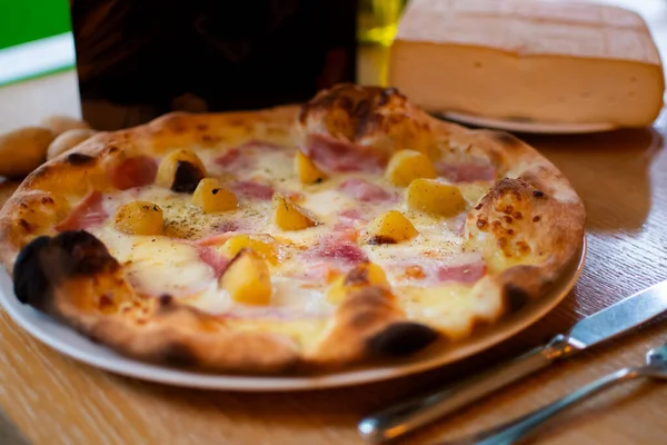 Hawaiian Pizza with pineapple, traditional italian oven baked dough with toppings: tomato sauce, cheese, mozzarella, ham. Simple brown wooden table restaurant setting