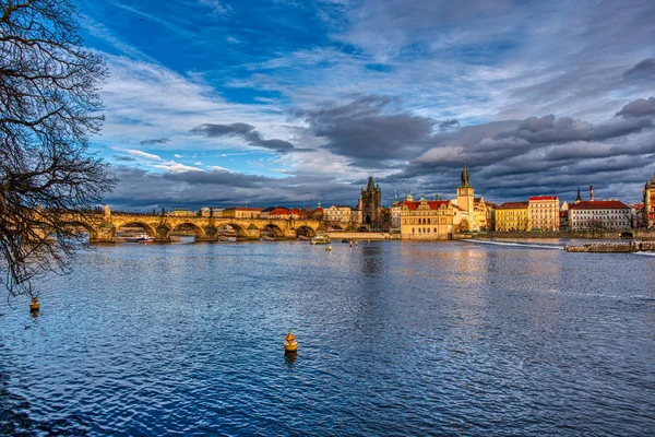 Ponte Charles lindamente iluminada ao pôr-do-sol com edifícios circundantes, Praga — Fotografia de Stock