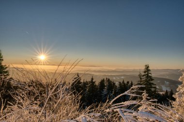 Altın güneş ışığı, arka planda küçük bir ahşap kulübesi olan cennet gibi beyaz bir kış manzarasının üzerinde.