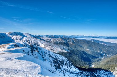 Tatra 'nın batısındaki dağların manzarası ve Slovakya' nın Low Tatras bölgesindeki tepeden gelen sisli ve mavi gökyüzü.