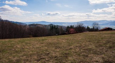 Dağlardaki çayırlarda üç eski kır evi ve arka plandaki dağ zirveleri, Polonya Beskids