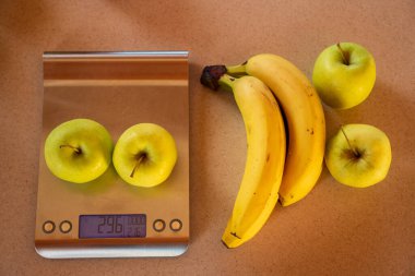 Elmalar dijital mutfak terazisinde ve yanında muz ve elmalar var.