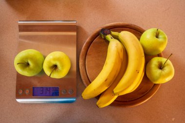 Elmalar dijital mutfak terazisinde ve yanında muz ve elmalar var.