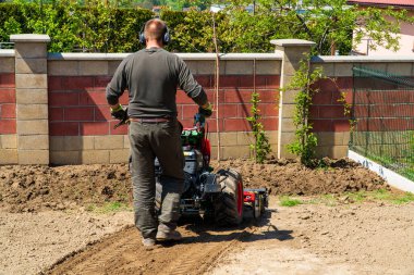 Adam bir motorlu ekiciyle toprağı sürüyor. Bir çiftçi petrol ekicisi kullanarak toprağı sürüyor..
