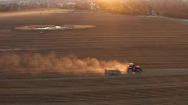 Aerial drone view of agricultural machinery in the foreground carrying out work in the field on sunrise morning — Stock Video
