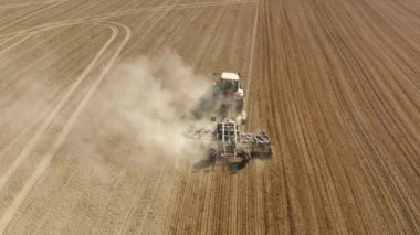 Traktör yağmur öncesi hazırlık için arazi ekme makinesini çekiyor. Bulutlu bahar günü. 4K hava sahayı