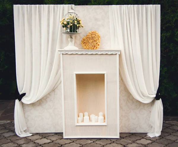 Fotozona de casamento em cores pastel: lareira, cortinas, velas, gaiola, buquê, coração de travesseiro . — Fotografia de Stock