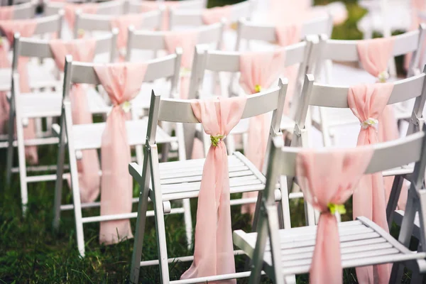 Cadeiras brancas na cerimônia de casamento, decoradas com um pano rosa . — Fotografia de Stock