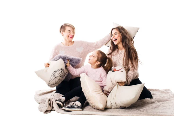 Mom and two daughters happily beat pillows and laugh.