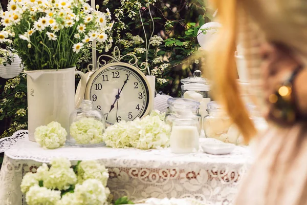 A mesa é decorada com branco, com relógios antigos, velas, flores, margaridas em um vaso. Um casal abraça-se . — Fotografia de Stock