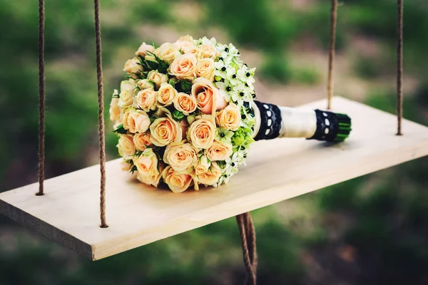 Um buquê de casamento de rosas está em um balanço de madeira na natureza — Fotografia de Stock