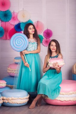 İki güzel kız mavi elbiseler eller büyük şeker ve Studio acıbadem kurabiyesi macaroons dekora tutun.
