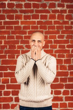erkek beyaz kazaklı backgraund tuğla duvarın üzerinde ağzını kapatır. Kopya alanı.