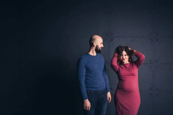 Бородатый мужчина улыбается, а беременная женщина касается волос, в студии на темном фоне. Копирование пространства . — стоковое фото