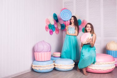 İki güzel kız mavi elbiseler eller büyük şeker ve Studio acıbadem kurabiyesi macaroons dekora tutun