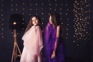 Neşeli kız. Pembe ve mor elbiseler Studio bokeh ile koyu arka plan üzerinde iki uzun saçlı kız. Kopya alanı.