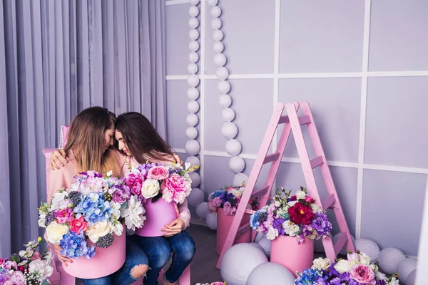 Duas meninas bonitas em jeans e suéter rosa no estúdio com decoração de flores em cestas . — Fotografia de Stock