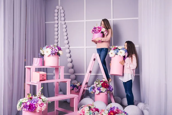 Duas meninas bonitas em jeans e suéter rosa no estúdio com decoração de flores em cestas . — Fotografia de Stock