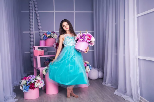 Hermosa chica en vestido azul en estudio con decoración de flores en cestas. Copiar espacio . — Foto de Stock