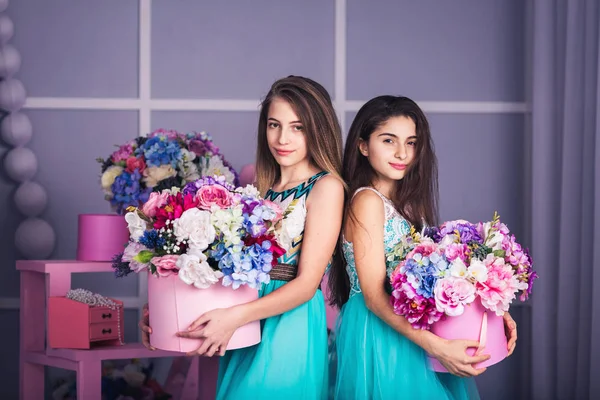 Dvě krásné dívky v modrých šatech ve studiu s dekorem květin v koších. — Stock fotografie