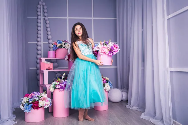 Hermosa chica en vestido azul en estudio con decoración de flores en cestas. Copiar espacio . — Foto de Stock