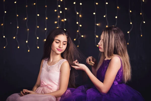 Des copines gaies. Deux filles se peignent les cheveux, assises côte à côte en studio sur fond sombre. Espace de copie — Photo
