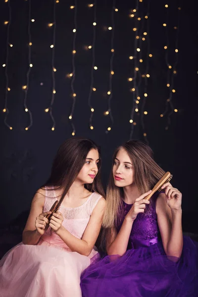 Des copines gaies. Deux filles se peignent les cheveux, assises côte à côte en studio sur fond sombre. Espace de copie — Photo