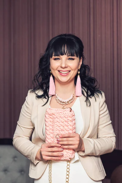 stylish girl in white dress and pink jacket with handmade pink earrings and knitted bag.