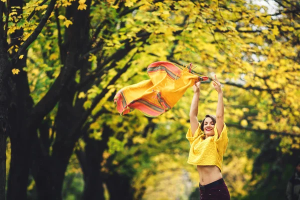 สาวสวยในฤดูใบไม้ร่วงในสวนโยนผ้าพันคอสีเหลืองขึ้นและยิ้ม . — ภาพถ่ายสต็อก