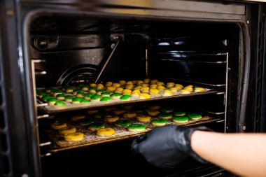 Pasta şefi fırına yuvarlak yeşil ve sarı ham eklerlerle birlikte fırın örtüsü koyar..