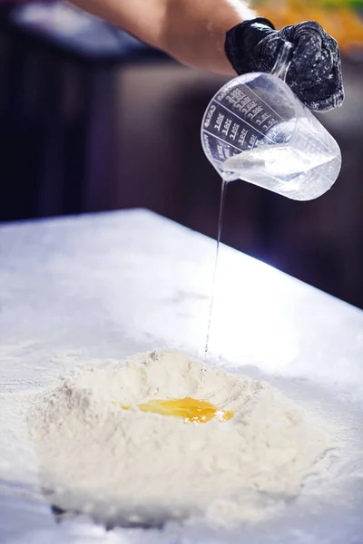 Baker adds water to heap of flour. — Stock Photo, Image