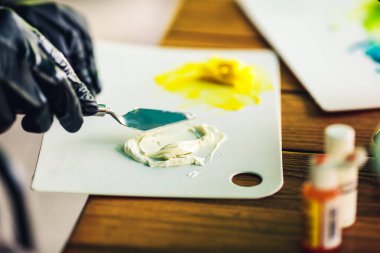 Siyah lastik eldivenli pasta şefi pastayı süslemek için renkli kremayı spatulayla karıştırıyor. Krema için gıda boyası.