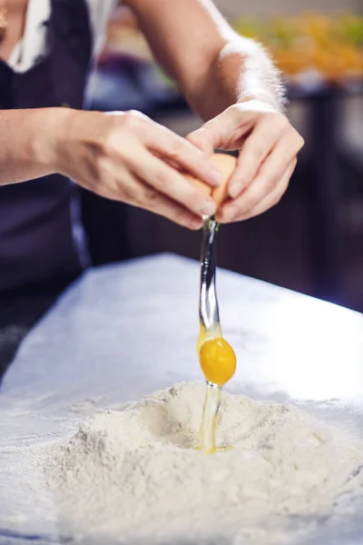 Baker breaks an egg into pile of flour. — Stock Photo, Image
