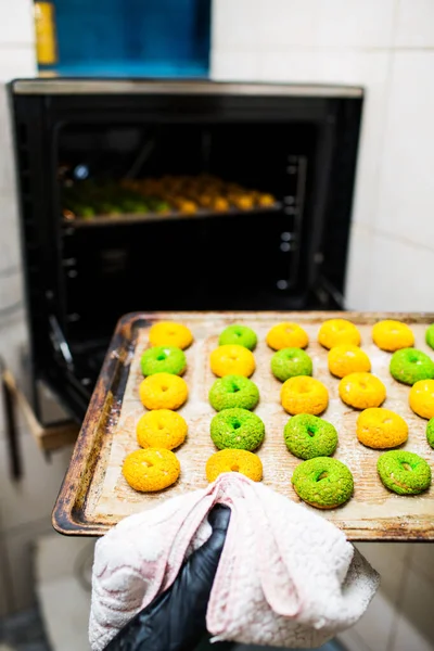 Confectioner takes out a baking sheet with round green and yellow eclairs from the oven. — Stock Photo, Image