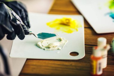 Siyah lastik eldivenli pasta şefi pastayı süslemek için renkli kremayı spatulayla karıştırıyor. Krema için gıda boyası.