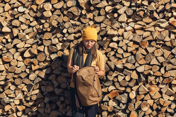 Toeristisch meisje staat in de buurt van stapel brandhout en opent rugzak. — Stockfoto