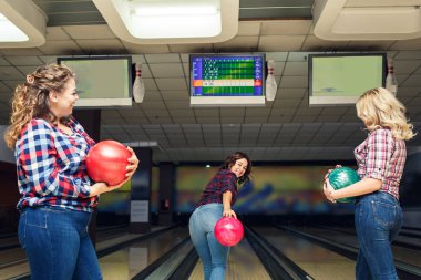 Üç neşeli çekici kız arkadaş toplarını tutar ve bowling oynarlar..
