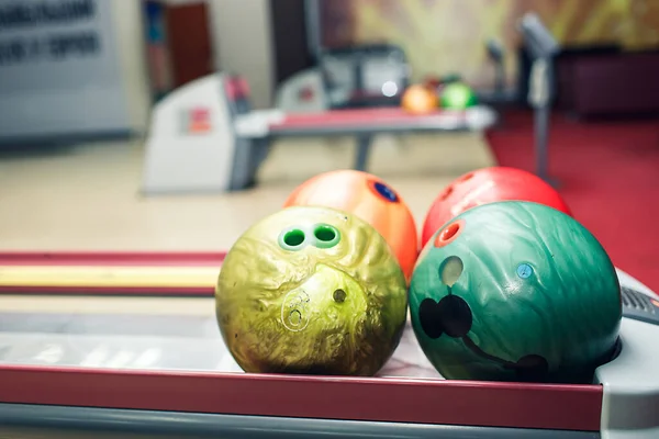 multi-colored bowling balls lie on shelf in bowling club.