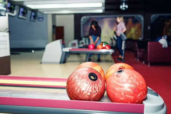 multi-colored bowling balls lie on shelf in bowling club.