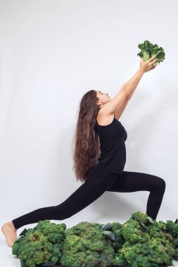 Sevimli atletik kız önünde koca bir kafa dolusu taze brokoli tutuyor ve yoga yapıyor..