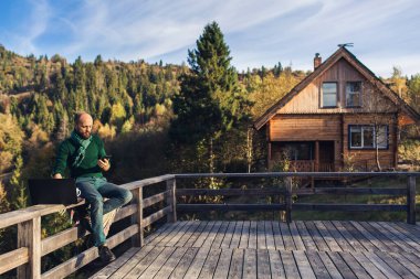 Sakallı adam dizüstü bilgisayarda çalışıyor, telefonla konuşuyor. Dağlarda tatilde olan serbest çalışan bir hippi.