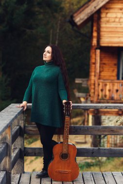 Gitarlı uzun saçlı bir kız. Log House 'un yanındaki terasta poz veriyor.