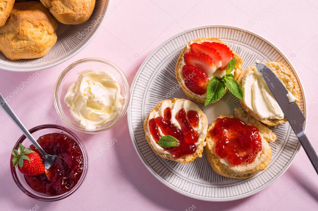 Tasty breakfast of scones with clotted cream and strawberry jam on pink background, top view
