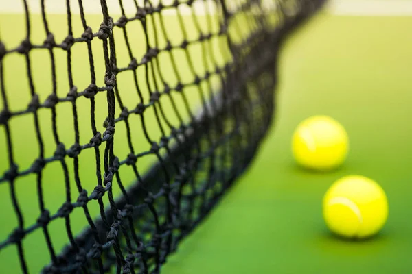Μαύρο συνυφασμένη net και δυο μπάλες του τένις στο πράσινο σκληρό δικαστήριο, εστίαση σε δίχτυ — Φωτογραφία Αρχείου